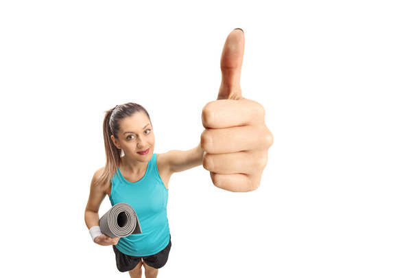 Fitness woman with an exercise mat making a thumb up sign isolated on white background - Foto, Bild