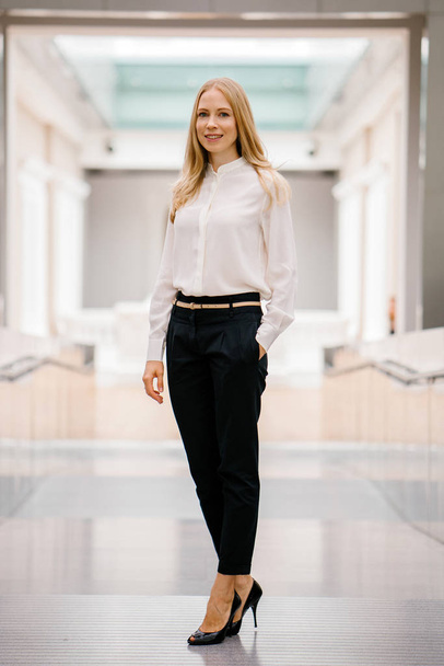full-length, full-body shot of an attractive mature Russian woman leader. She is elegantly dressed in professional white shirt and black pants and heels and is smiling confidently. - Foto, Bild
