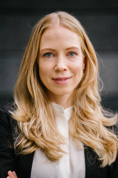 Portrait of a Caucasian, white and attractive middle-aged woman in a professional suit against a dark grey background. She is beautiful with blond hair and blue eyes and smiling for her head shot. - Foto, afbeelding