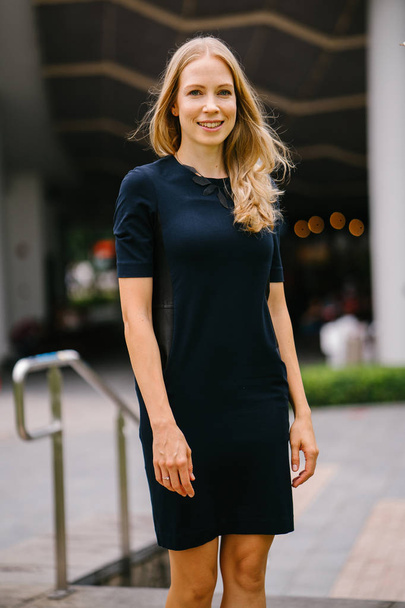 Portrait of a very beautiful white Caucasian woman in a black dress. She is blond with blue eyes, middle-aged, attractive, beautiful and smiling. She is a Russian expatriate living in Singapore. - Foto, afbeelding
