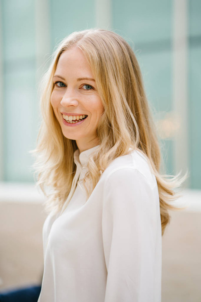 Professional portrait head shot of a Caucaasian woman expatriate working in Singapore, Asia. She is middle-aged in her 30's, attractive, blond and beautiful in a crisp white shirt in an office. - Valokuva, kuva