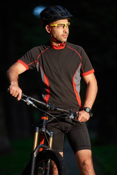 Smiling male standing cyclist near bike, happy to begin morning with training. Sportsman having fun exercising outdoors. Concept of healthy lifestyle, new beginning - Photo, Image