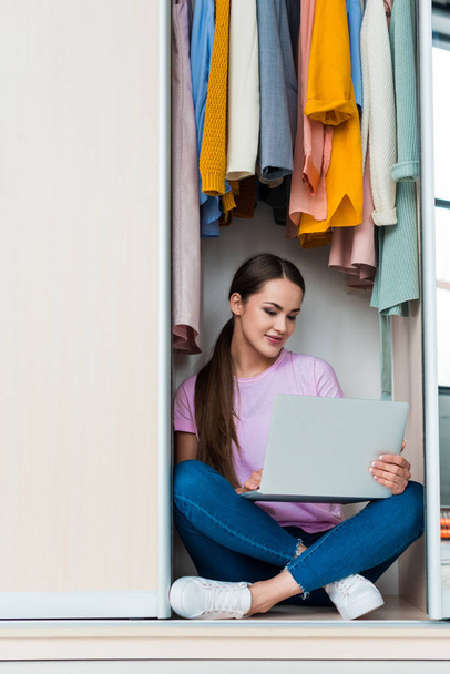 happy young woman sitting inside of cabinet and working with laptop at home - Foto, Bild