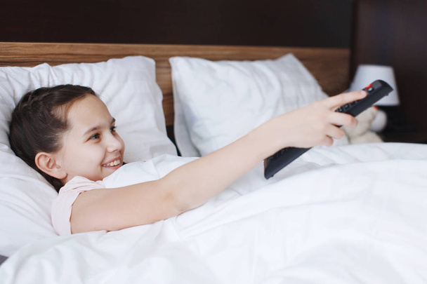 Молода мила дівчина лежить в ліжку з білим одягом і дивиться на камеру
 - Фото, зображення