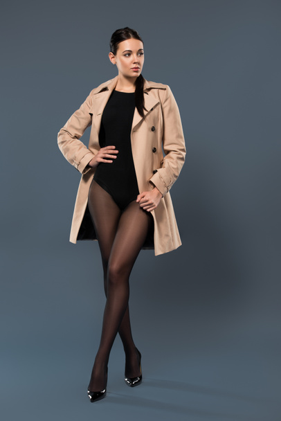 Woman posing in black pantyhose and beige trench on dark background - Foto, Bild
