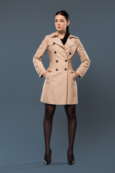 Young woman in black tights and beige trench on dark background - Photo, image