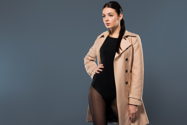 Woman in black pantyhose and beige trench isolated on dark background - Фото, изображение