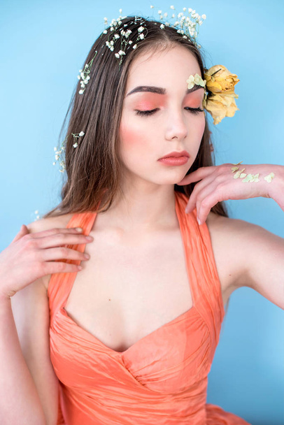 Cosmetics and manicure. Close-up portrait of attractive woman with dry flowers on her face and hair, pastel color, perfect make-up and skin on blue background. Fresh, trendy, spring retouched portrait - Valokuva, kuva