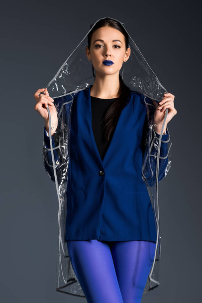Attractive woman in blue jacket and transparent raincoat isolated on dark background - Foto, Imagem