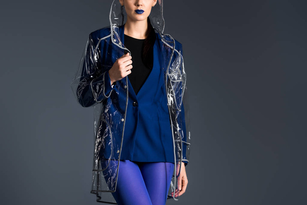 Woman posing in blue jacket and transparent raincoat isolated on dark background - Фото, изображение
