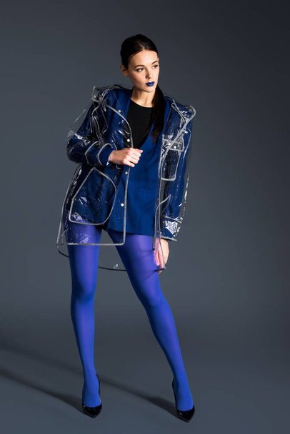 Young girl with blue lipstick wearing transparent raincoat on dark background - 写真・画像