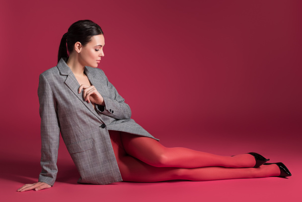 Slim woman in red pantyhose and grey jacket lying on red background - Photo, Image