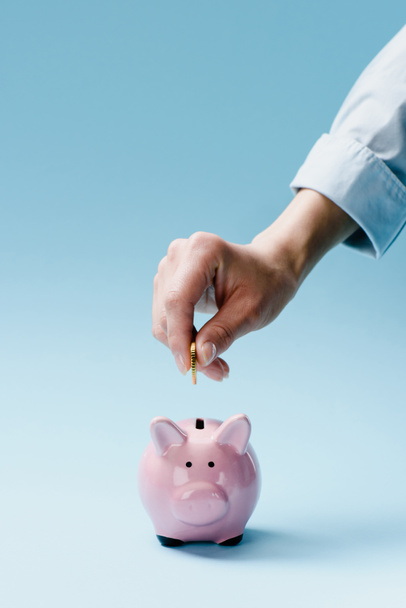 visão parcial do homem colocando moeda em rosa porquinho banco isolado em azul
 - Foto, Imagem