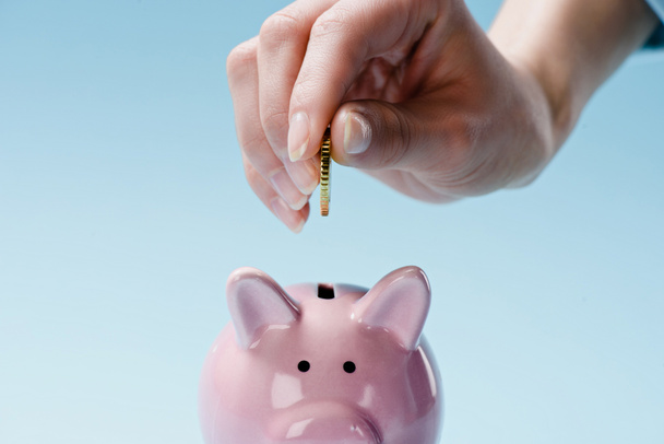 partial view of woman putting coin into pink piggy bank isolated on blue - Photo, Image