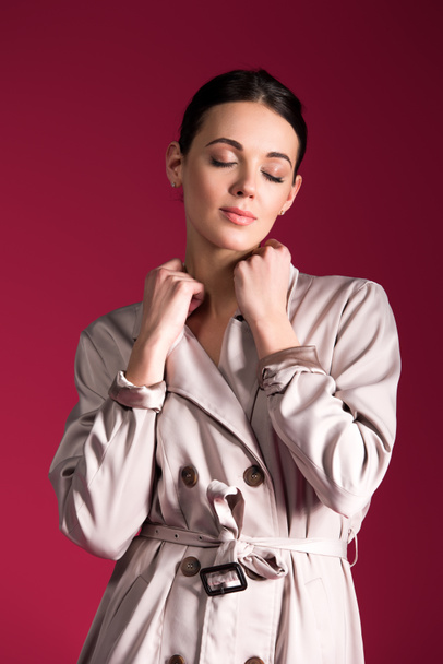 Dreamy girl wearing beige trench isolated on red background - Foto, Bild
