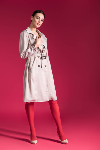 Smiling girl wearing beige trench and high heels on red background - Foto, Imagem