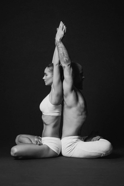 Zwart-wit portret van mooie sportieve paar: vrouw en man in de witte kleren doen yoga asana's elkaar binnen  - Foto, afbeelding
