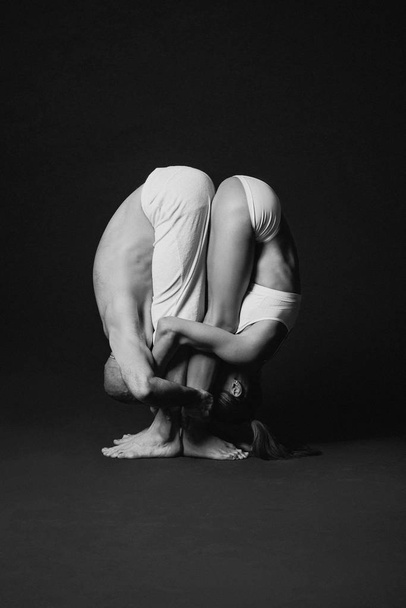 Monochrome portrait of beautiful sporty couple: woman and man in white clothes doing yoga asanas together indoor  - Foto, immagini