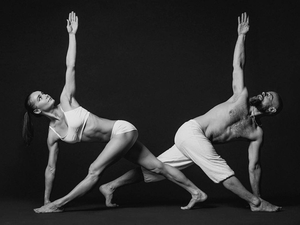 Monochrome portrait of beautiful sporty couple: woman and man in white clothes doing yoga asanas together indoor  - Φωτογραφία, εικόνα