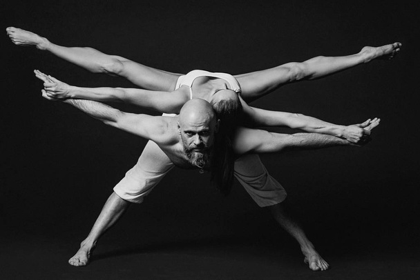 Retrato monocromático de hermosa pareja deportiva: mujer y hombre en ropa blanca haciendo asanas de yoga juntos en interiores
  - Foto, Imagen