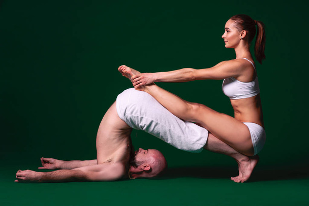 Beautiful sporty woman and man in white clothes doing yoga asanas together indoor on green background - Photo, Image