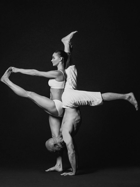 Монохромный портрет красивой спортивной пары: женщина и мужчина в белых одеждах вместе занимаются асанами йоги в помещении
  - Фото, изображение