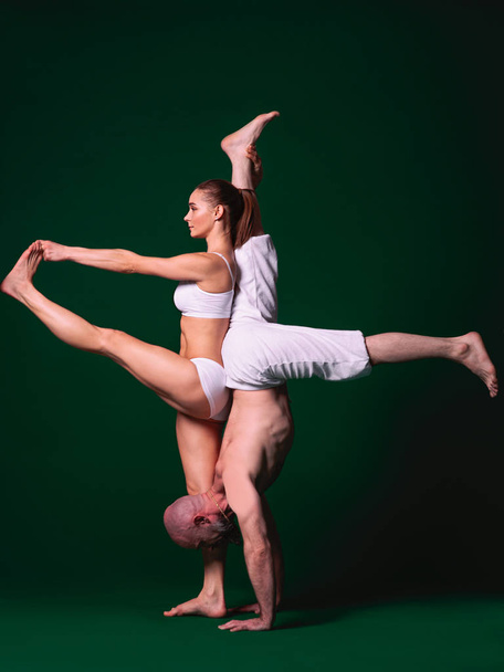 Beautiful sporty woman and man in white clothes doing yoga asanas together indoor on green background - Foto, Imagem