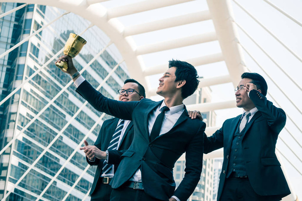 Ευτυχισμένος ασιατικές επιχειρήσεις τους ανθρώπους με χρυσή κυπέλλων για τους νικητής στο επιχειρηματικό σχέδιο. Ομαδική εργασία και την επιτυχία έννοια - Φωτογραφία, εικόνα
