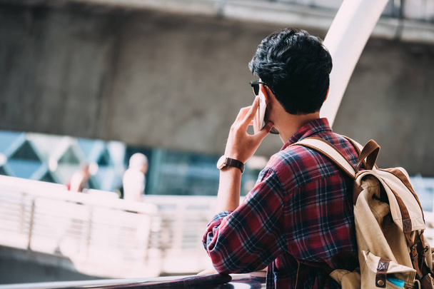 Casual jeune asiatique homme avec sac à dos parler sur téléphone mobile dans la ville
. - Photo, image
