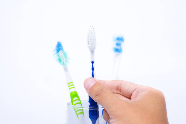 Hand holding new toothbrush and old toothbrush (damaged) in clear glass for teeth cleaning isolated on white background - concept "How often should you change your toothbrush ? " - Photo, Image