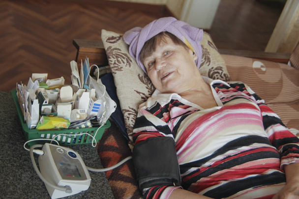 病気の年配の女性は圧力を測定するためのタブレットおよび装置とベッドに横たわっている - 写真・画像