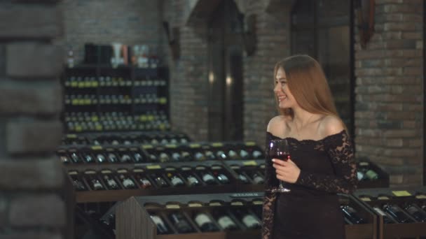 Er is een mooi meisje in een wijnkelder. Slow-motion. Een lief meisje met een glas rode wijn is lacht. - Video