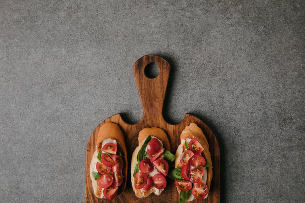top view of gourmet italian bruschetta on wooden cutting board on grey   - Φωτογραφία, εικόνα