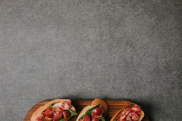 top view of delicious italian bruschetta on wooden board on grey background - Zdjęcie, obraz