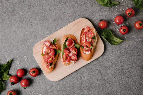 top view of delicious bruschetta on wooden board and fresh ingredients on grey - Foto, afbeelding