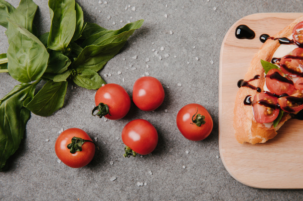 top view of delicious bruschetta on wooden board, basil and fresh tomatoes on grey     - Foto, afbeelding