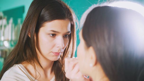 Styliste professionnel femme faisant maquillage pour jeune femme devant le miroir dans le salon de beauté
 - Photo, image