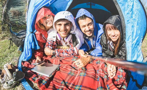 Best friends couples taking selfie at camping tent on sunny day after the rain - Youth and freedom concept outdoors in spring break vacation - Young people having fun traveling together - Warm filter - Photo, Image