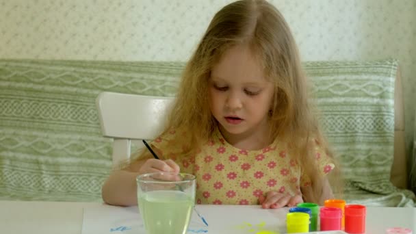 mooie roodharige meisje schildert met paintand borstel zittend aan tafel - Video