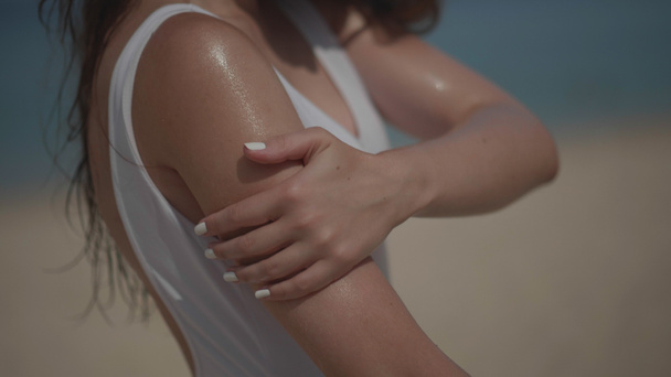 Belle fille en maillot de bain appliquant crème solaire huile bronzante sur le corps sur la plage de sable tropical pendant les vacances d'été sur fond de mer et de ciel
 - Photo, image