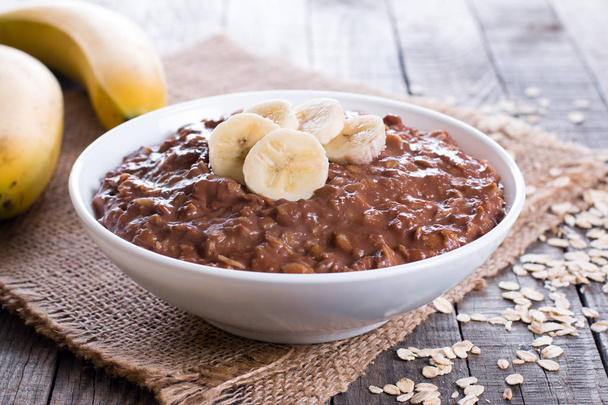 Chocolate oatmeal with banana in white bowl for breakfast - Photo, Image
