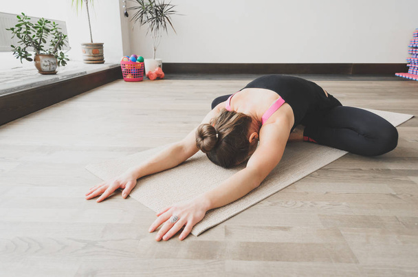 Woman makes the yoga exercise on the mat, indoors - Valokuva, kuva