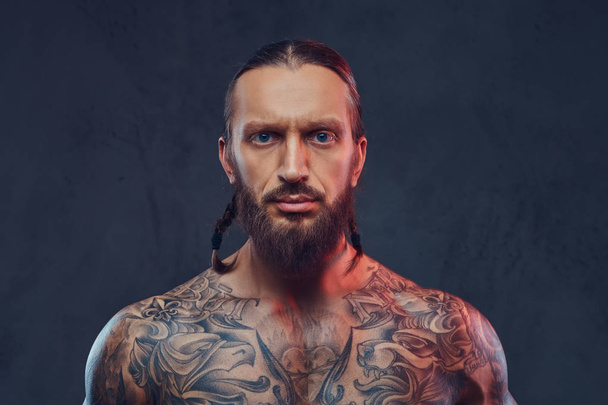 Retrato de close-up de um macho tatuado de barba muscular com um corte de cabelo elegante. Isolado em um fundo escuro
. - Foto, Imagem