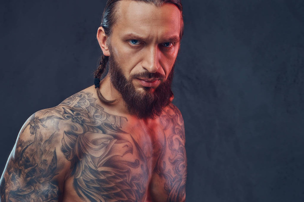 Крупный план портрета мускулистого бородатого татуированного мужчины со стильной стрижкой. Изолированный на тёмном фоне
. - Фото, изображение