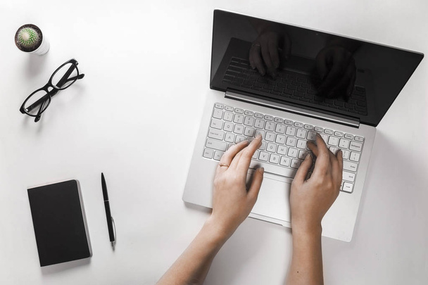 Vrouwelijke handen tekst afdrukken op laptop. Bovenaanzicht van moderne werkruimte met laptop, cactus, brillen, notebook en pen. - Foto, afbeelding