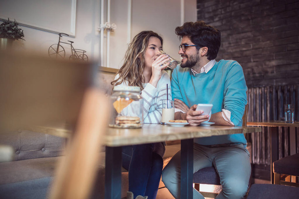 Loving couple sitting in cafe drinking coffee and using phone.  - Valokuva, kuva