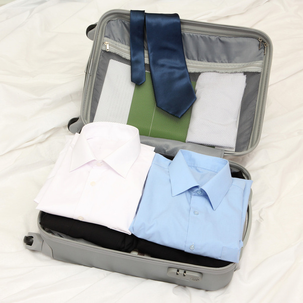 Open grey suitcase with clothing on bed - Valokuva, kuva