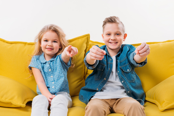little boy driving and sister pointing while sitting on yellow sofa  - Photo, Image
