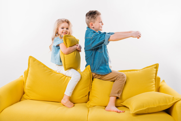 poika teeskentelee olevansa kuljettaja istuessaan keltaisella sohvalla siskon kanssa
 - Valokuva, kuva