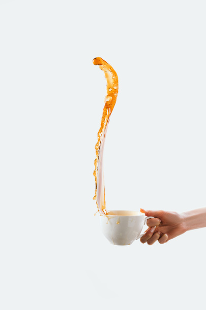 cropped view of hand holding big white cup with splash of coffee, isolated on white - Photo, image